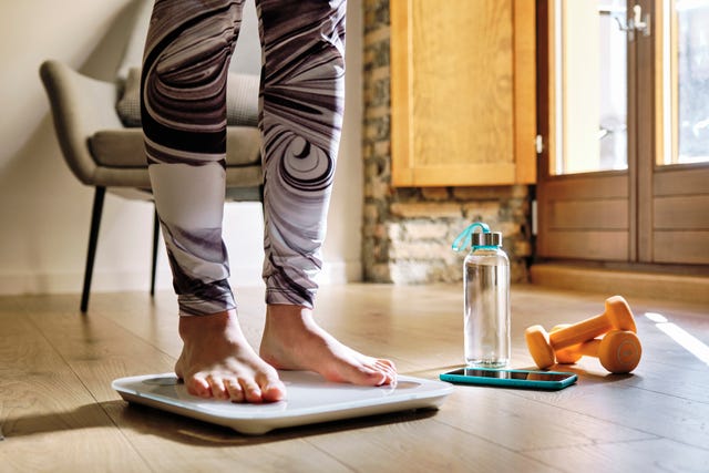 woman analyzing weight while standing on weight scale at home