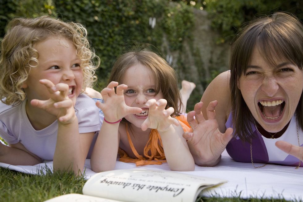 a woman and two girls growling and holding their hands up like claws while lying down in a backyard