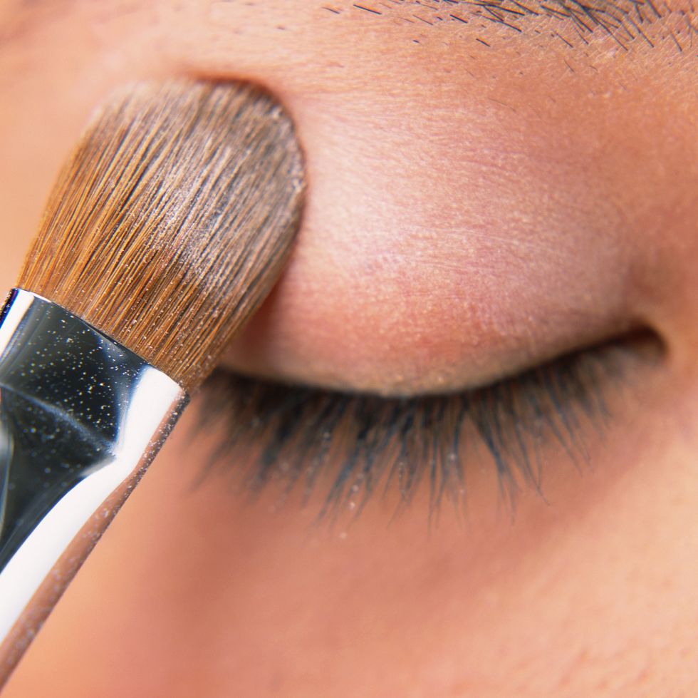 a woman applying beige colored eye shadow, front view, differential focus