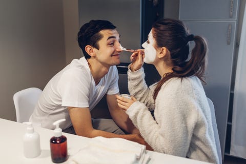 Woman applying clay mask on her boyfriend's face. Young loving couple taking care of skin at home woman applying clay mask on her boyfriend's face