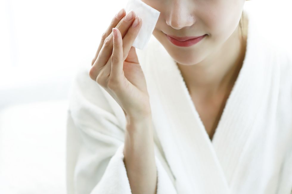 Woman applying cleansing lotion to face, using cotton wool pad