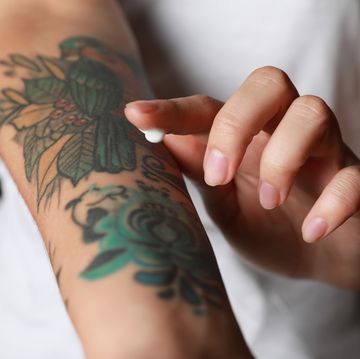 woman applying cream on her arm with tattoos against black background, closeup