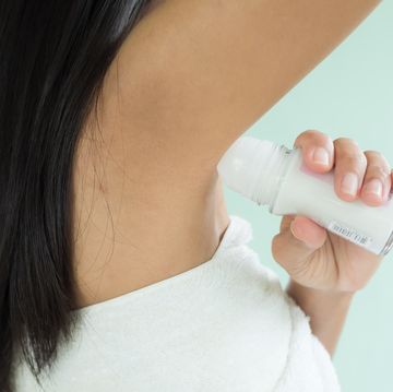 woman applying deodorant roll on under armpit after shower