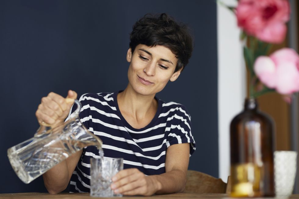 Woman at home sitting at wooden table pouring water into glass