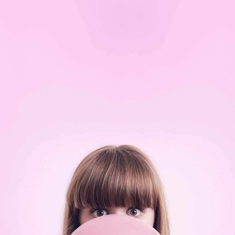 caucasian woman blowing large bubble gum bubble on pink background