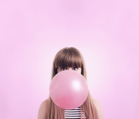 caucasian woman blowing large bubble gum bubble on pink background