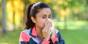 woman blowing her nose on a tissue outdoors