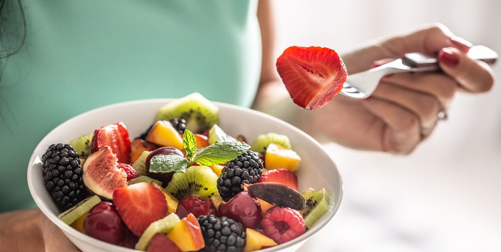a woman breakfasts a fruit salad high in vitamins and fiber