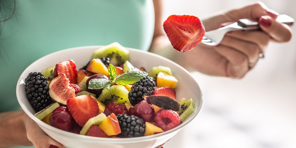a woman breakfasts a fruit salad high in vitamins and fiber