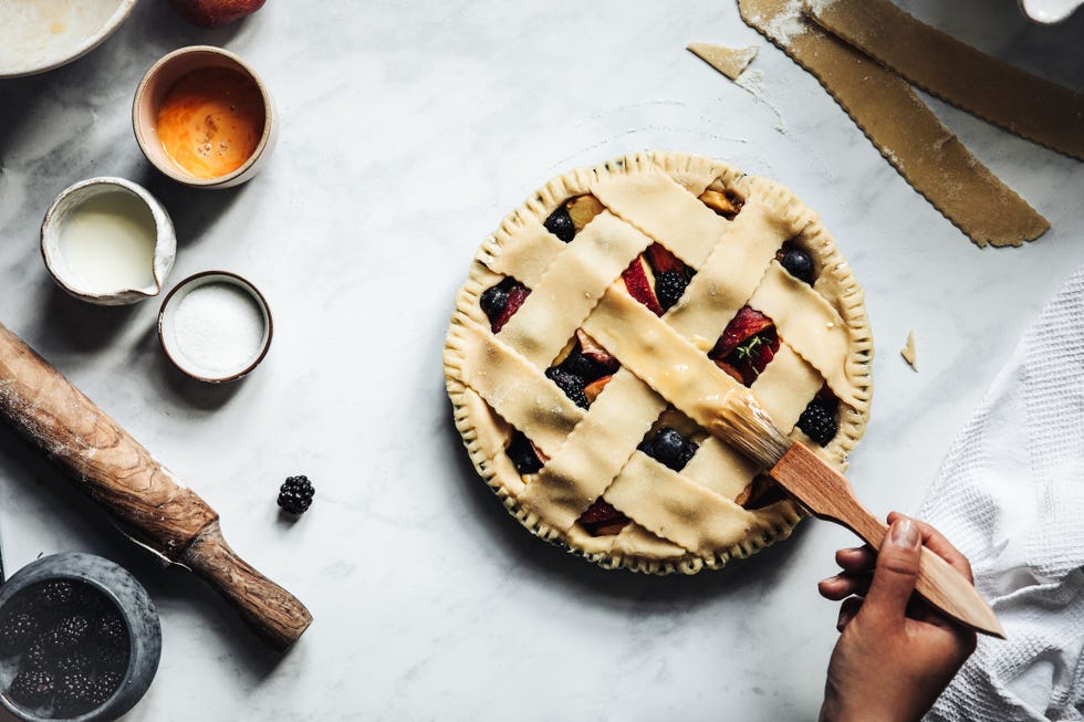 una mano coge una brocha para dorar con huevo una tarta de frutas