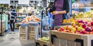 Woman buying oranges while carrying shopping basket in supermarket