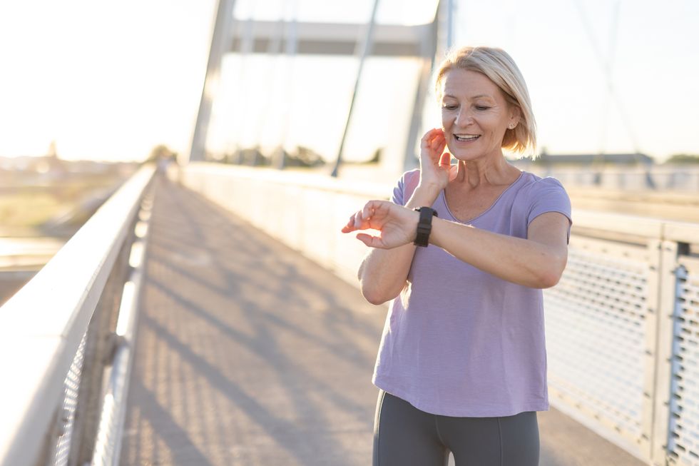 woman checking smartwatch on bridge during workout under sunlight