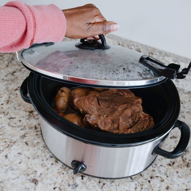 woman checks on food in slow cooker