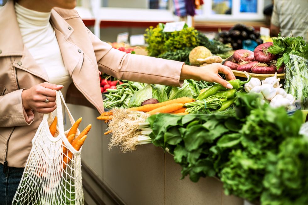 woman choosing greenery and vegetables at farmer market and using reusable eco bag