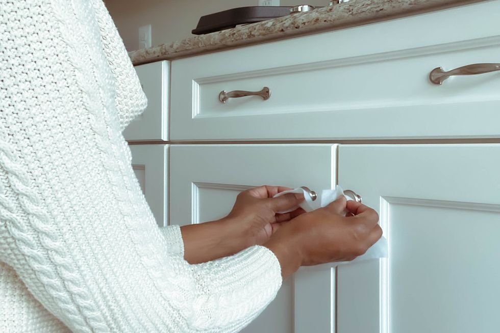 woman cleans cabinet hardware using disinfectant wipe
