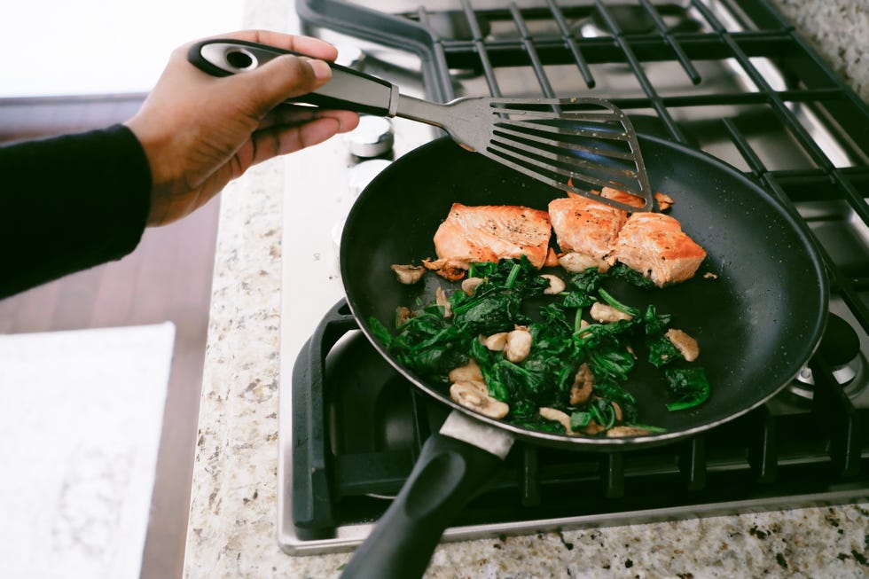 woman cooks salmon with spinach and mushrooms