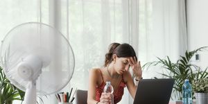woman at desk cooling herself with an electric fan