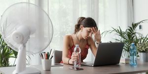 woman at desk cooling herself with an electric fan