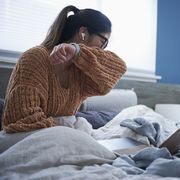 woman coughing into elbow while sitting in bed