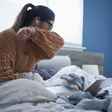 woman coughing into elbow while sitting in bed