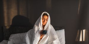 woman wrapped in blanket in bed holding a hot drink