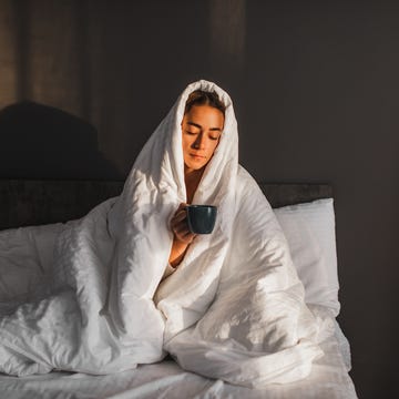 woman covered in blanket enjoying hot morning coffee in bed in cold morning