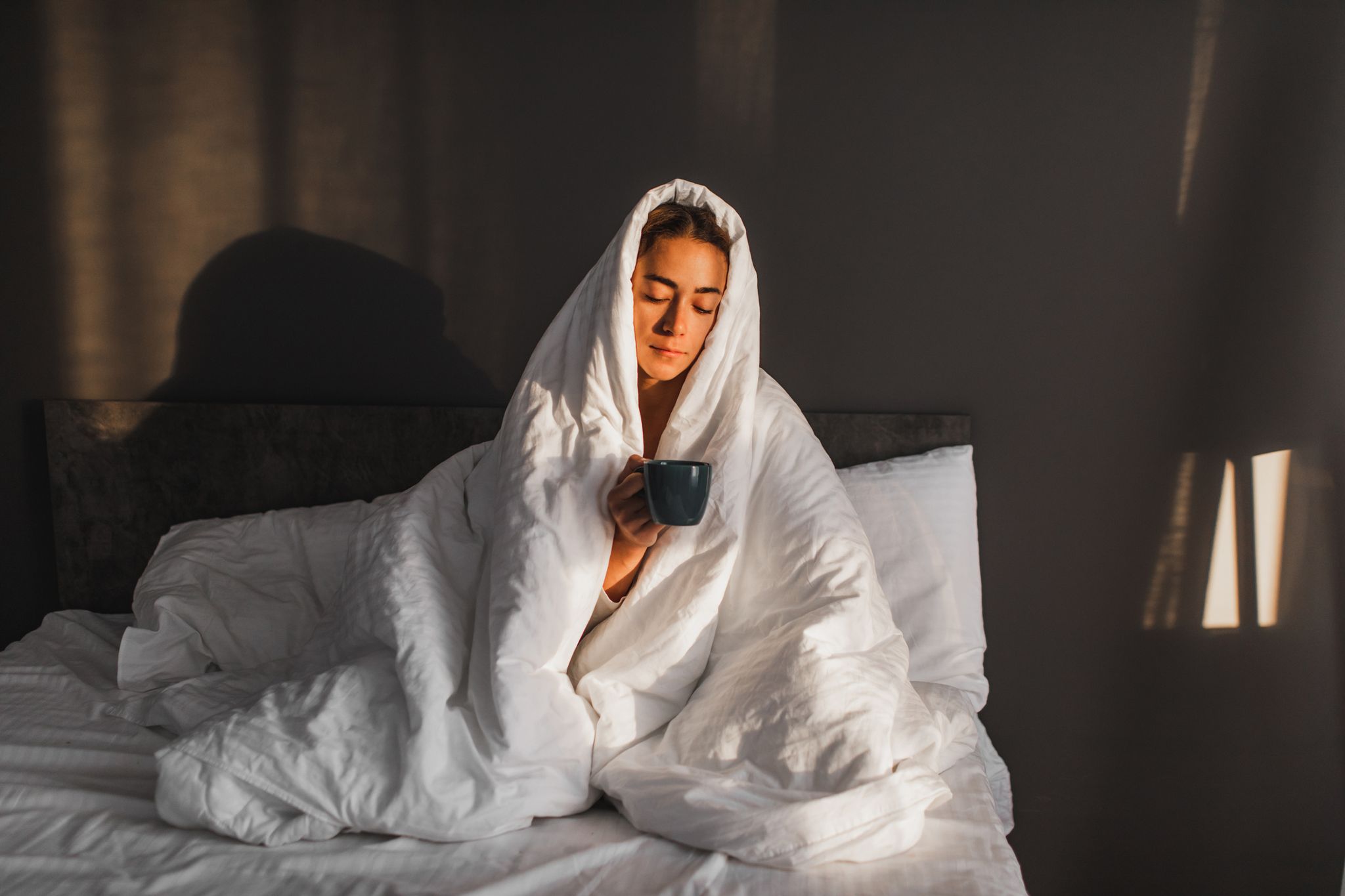 woman covered in blanket enjoying hot morning coffee in bed in cold morning