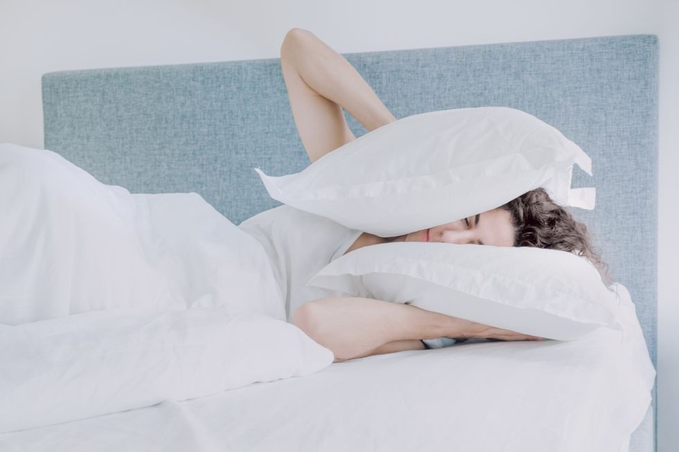 woman covering ears with pillows while sleeping on bed