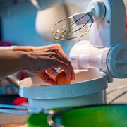 woman cracking egg into stand mixer to make donuts dough