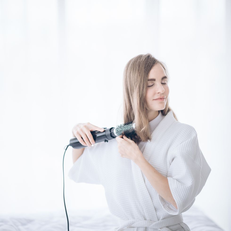 woman curling hair on bed at home