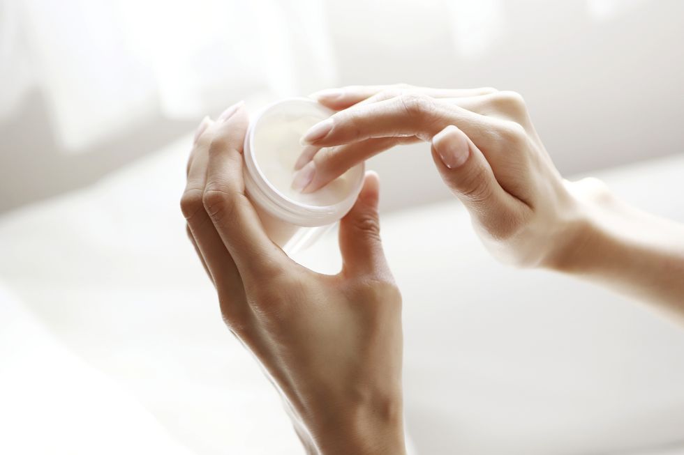 woman dipping finger in moisturizer jar