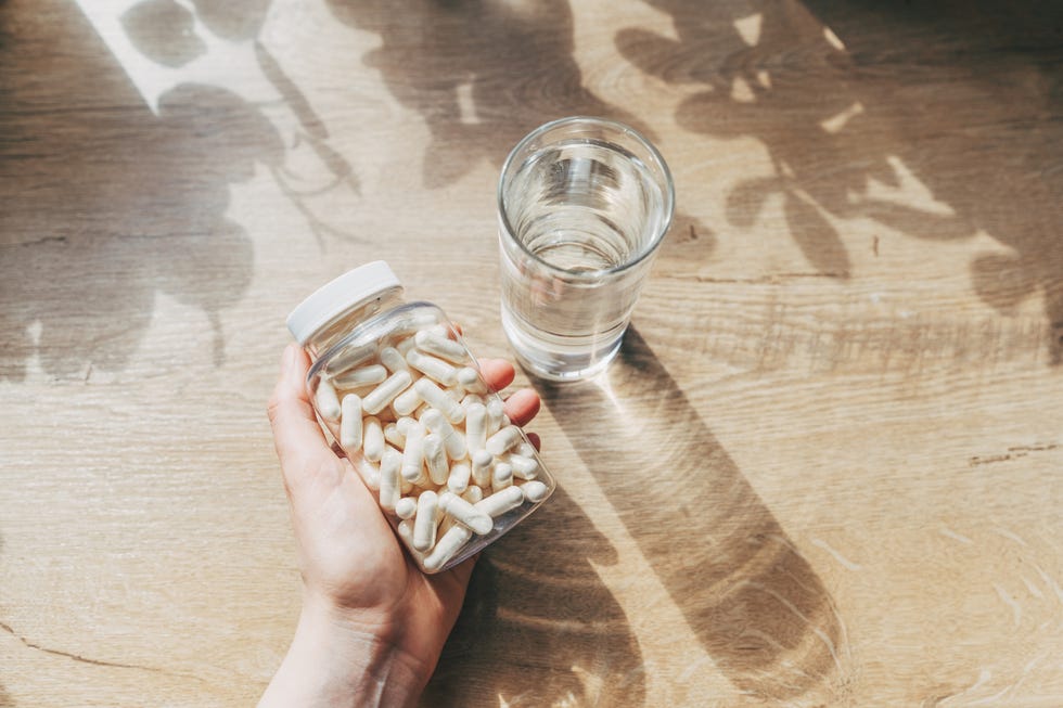 bottle of multivitamins with a hand on a wooden table