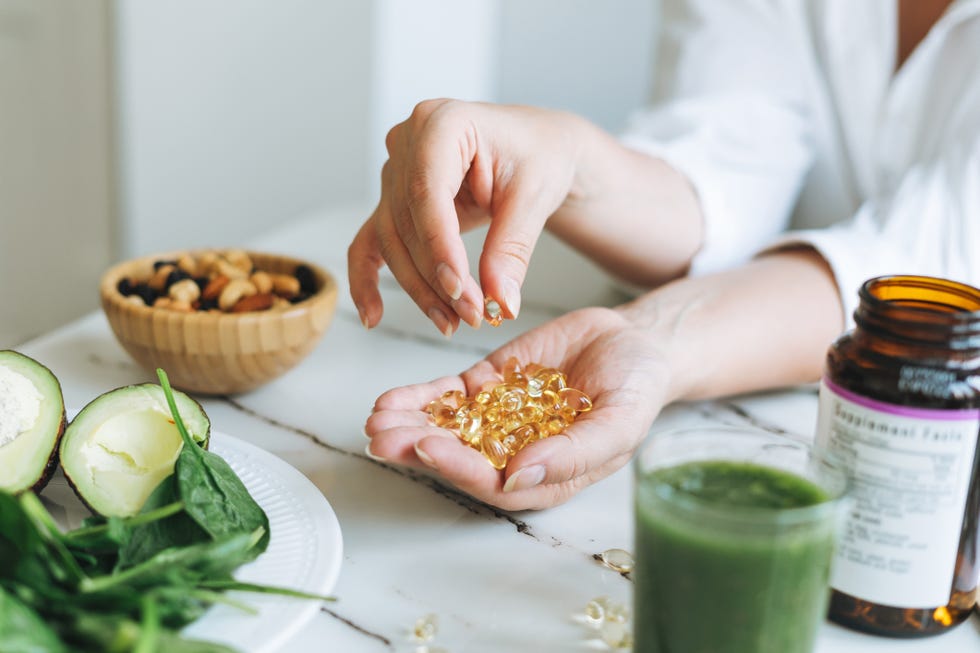 woman doctor nutritionist hands in white with omega 3, vitamin d capsules with green vegan food