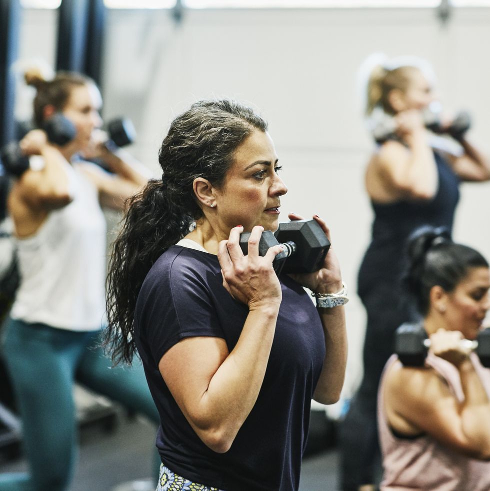 woman doing dumbbell squats during fitness class in gym