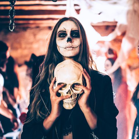 young woman with santa muerte make up and disguise holding skull at halloween party