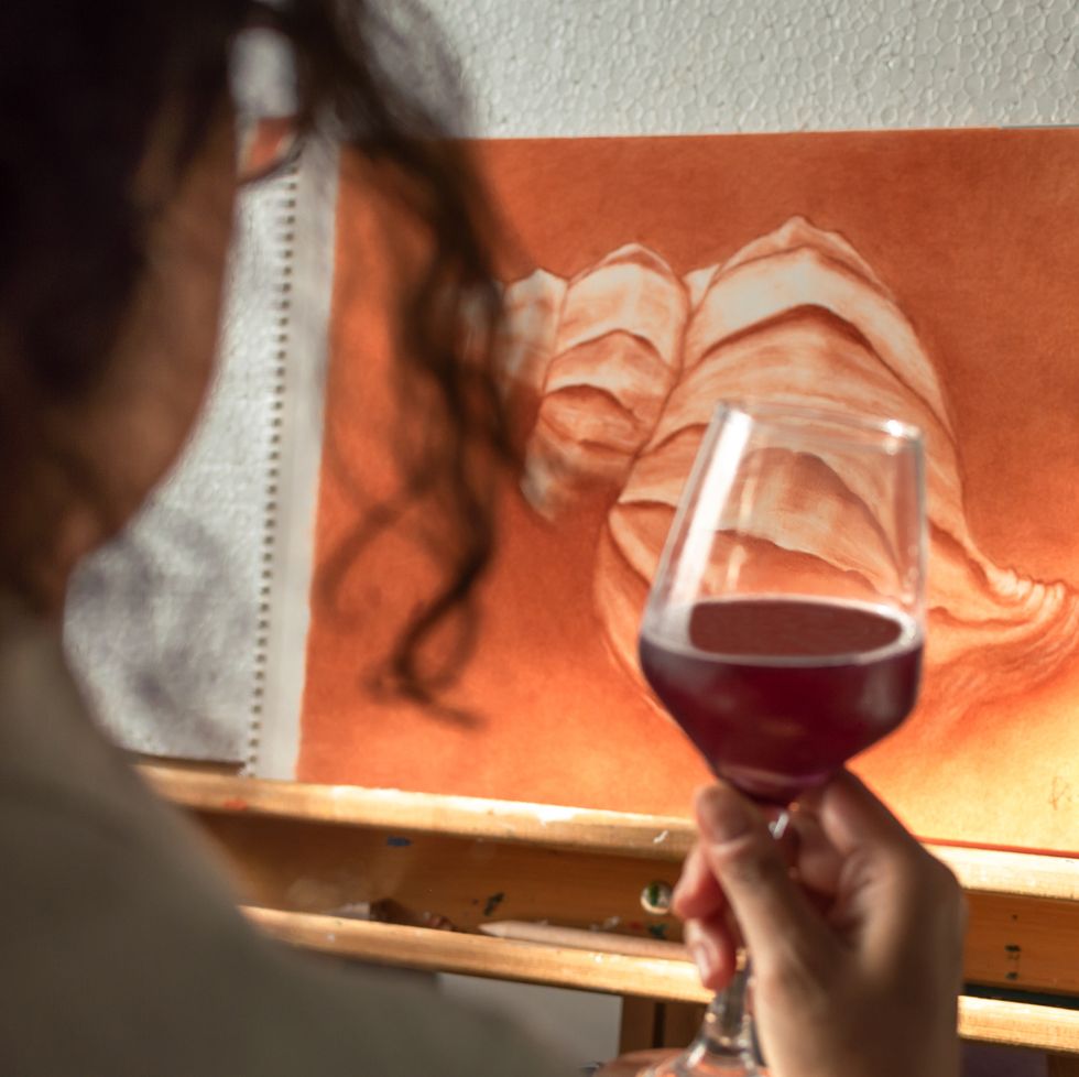 woman drinking a glass of wine to celebrate that she has finished her painting artist contemplating his finished work