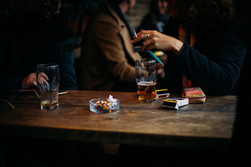woman drinking alcohol, smoking cigarettes, and holding a mobile phone in a pub