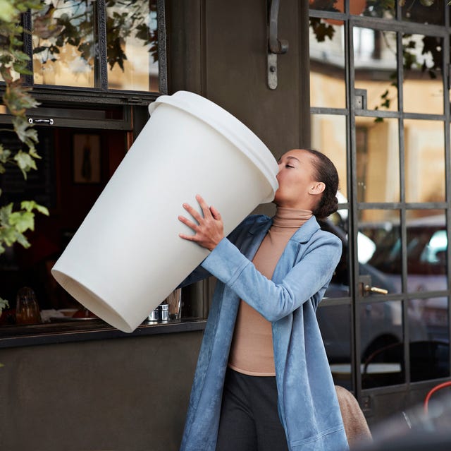 woman drinking coffee from large disposable cup at take away counter of cafe