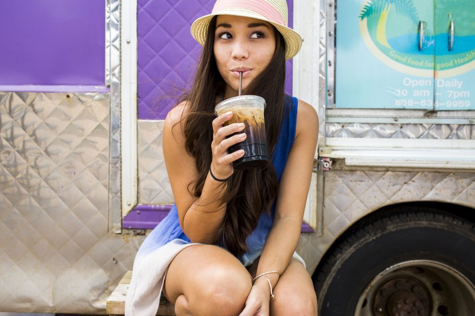 woman drinking ice coffee near food cart