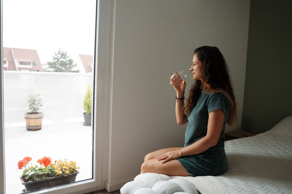woman drinking water while sitting on a bed smiling