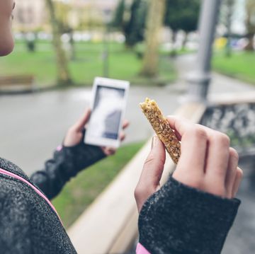 Woman eating cereal bar after training and holding smart phone