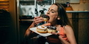 Woman eating donuts in front of the refrigerator late night