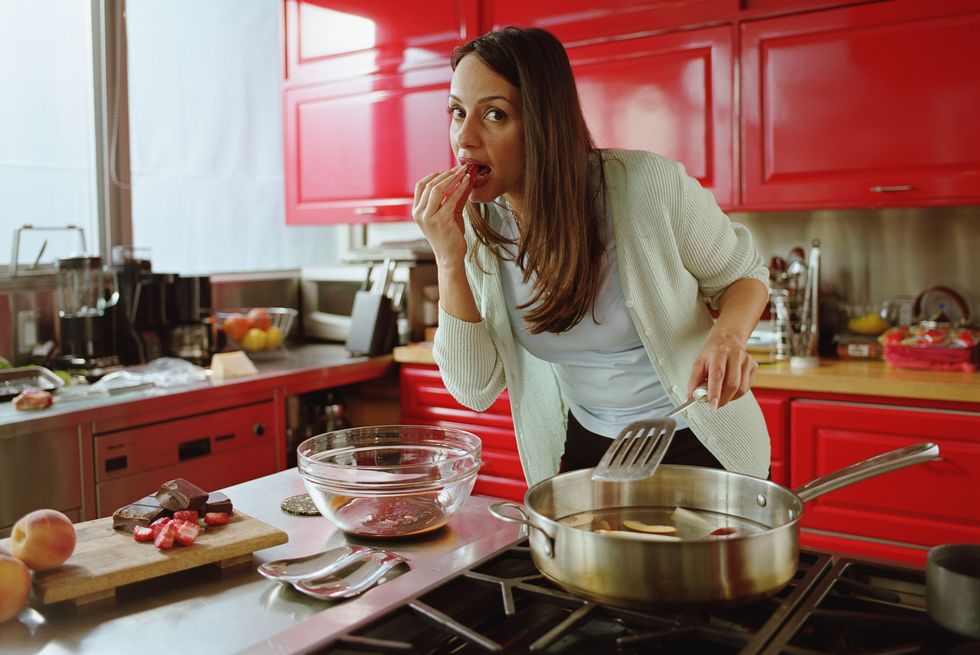 woman eating strawberry while cooking in kitchen