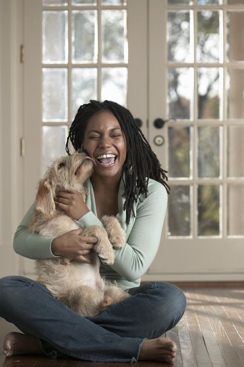 woman embracing dog sitting on floor, dog licking woman's face