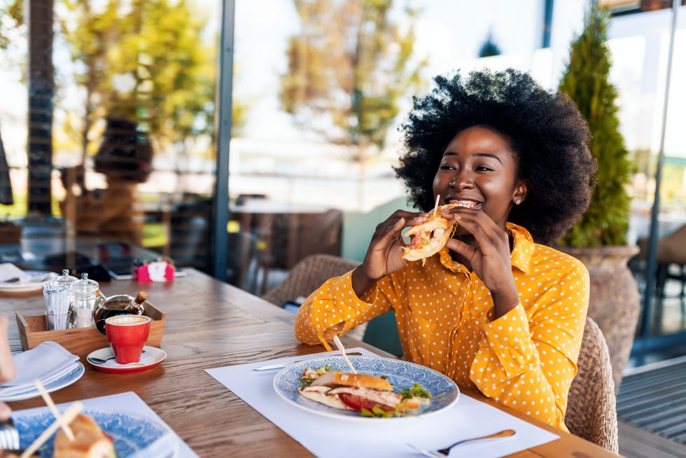 woman enjoying eating sandwich at restaurant