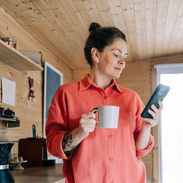 woman enjoying morning coffee and checking her phone in rustic kitchen