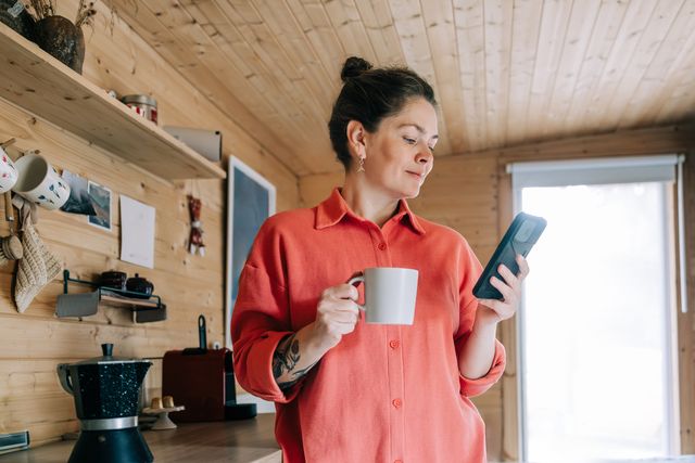 woman enjoying morning coffee and checking her phone in rustic kitchen