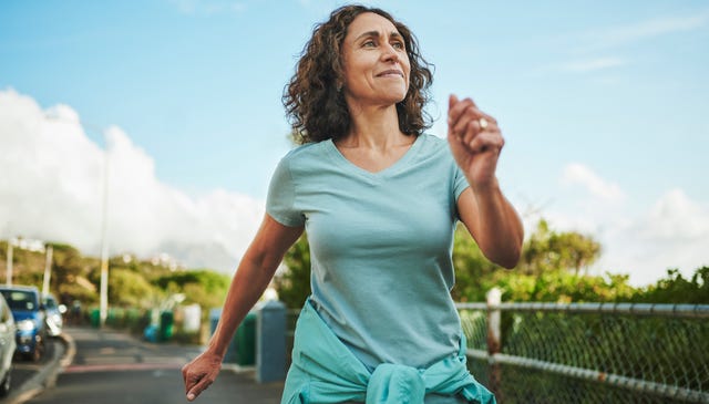 mature woman in sportswear smiling while out for a power walk along a sidewalk outside in summer