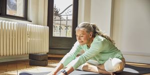 woman exercising while sitting on exercise mat over floor in living room