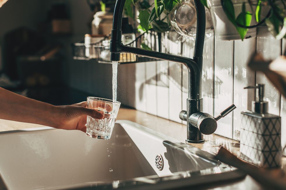 woman filling glass with water from tap in kitchen, closeup